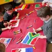 photo  les élèves de la petite section ont préparé des drapeaux de différents pays dont ils achèvent le coloriage. 