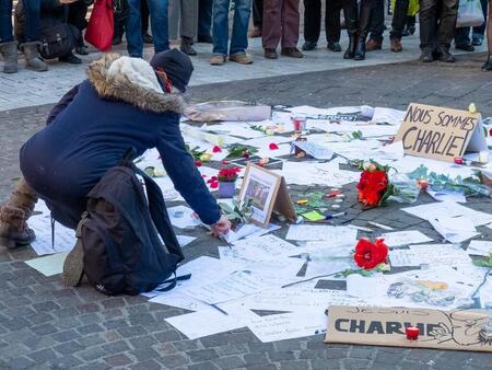 photo Au lendemain des attentats de Charlie Hebdo du 7 janvier 2015, à Paris, une personne dépose une fleur à côté des messages et des fleurs déposés sur le sol en hommage aux victimes dans une rue de Grenoble. FREDERIC MOREAU / Hans Lucas via AFP 
