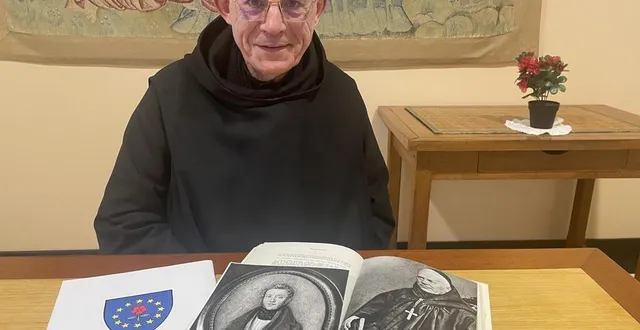 photo  le père jacques-marie guilmard devant le blason de l’abbaye et des portraits de dom guéranger, jeune homme puis moine âgé.  &copy;  le maine libre 
