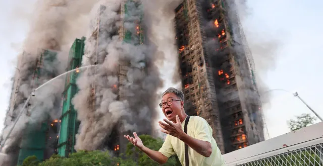 photo  wong, 71 ans réagit alors que son épouse est coincée dans l’un des immeubles dévorés par les flammes. de la fumée s’élève des échafaudages en bambou sur plusieurs bâtiments du complexe résidentiel wang fuk court, à tai po, hong kong, chine, le 26 novembre 2025.  &copy;  tyrone siu / reuters 