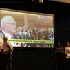 photo  après la projection du film, les conseillers municipaux, sur scène, chantent une chanson au maire. 
