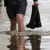 photo  un homme marche dans l’eau avec des bottes dans une main. photo d’illustration. 