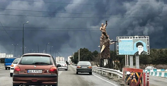 photo  des véhicules circulent sur une autoroute, passant devant une statue commémorative de guerre et un panneau d’affichage représentant le défunt guide suprême iranien, l’ayatollah ali khamenei, tué lors d’une frappe aérienne le 28 février, avec des panaches de fumée noire qui s’élèvent, à téhéran le 8 mars 2026.  &copy;  afp 